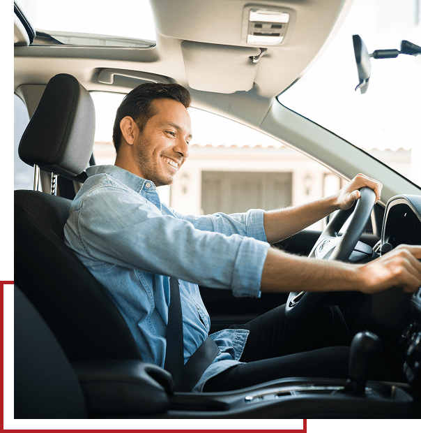 A man in a blue shirt smiles while driving a car.